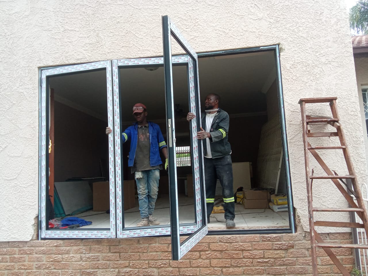 Workers fitting a large aluminium folding door frame into a wall opening