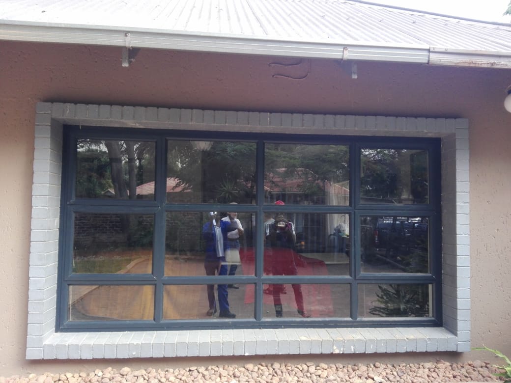 Wide dark aluminium multi-pane window installed under a corrugated roof